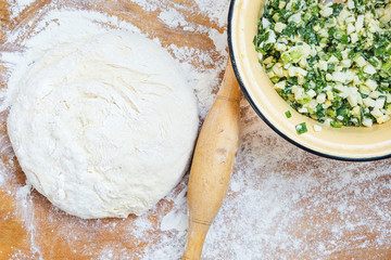 Rolling pin, dough and filling for the cake on a wooden background. Minced green onions and eggs.