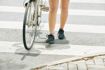 Fit legs of young woman standing on crossing road with her bicycle
