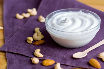 Fototapeta na wymiar Closeup of bowl with organic yoghurt on purple linen napkin. Low calorie diet breakfast of dairy products with nuts for good digestion and functioning of gastrointestinal tract. Healthy food concept.