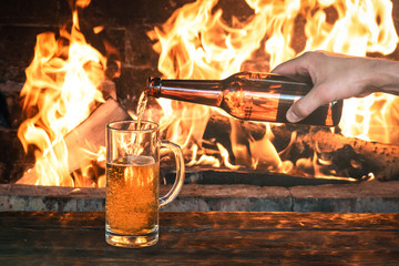 Man hand is pouring a beer from a bottle to a transparent glass on a burning fire background.