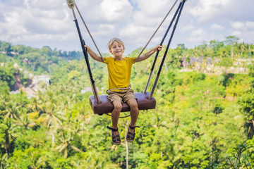 Young boy swinging in the jungle rainforest of Bali island, Indonesia. Swing in the tropics. Swings - trend of Bali. Traveling with kids concept. What to do with children. Child friendly place