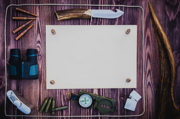 Hunting knife, binoculars, ammo for the carbine and the flask of brandy. The horn of Elk or Reindeer on a wooden background. A sheet of old paper for your text