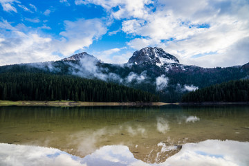Montenegro, Reflecting mountain bobotov kuk snow covered behind green forest and clouds mirroring in black lake water in durmitor national park nature landscape near zabljak