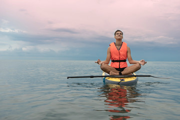 Surf man in life jacket does yoga and meditation on a sup surfboard, Concept safety on the water