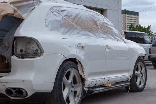 The car after the accident in the workshop for body repair is partially covered with paper and pasted over with masking tape for painting the side doors and the fender with white color