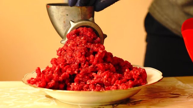 Close up shot of beef meet being minced in the manual retro mince machine. Hands of unrecognizable person with blue gloves filling up machine and rotating handle