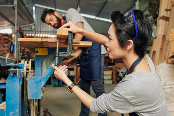 Female carpenter adjusting workbench and her coworker putting wooden plank on table to cut it in pieces