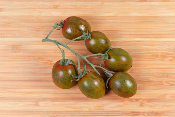 Cluster of cherry tomatoes kumato on the bamboo cutting board