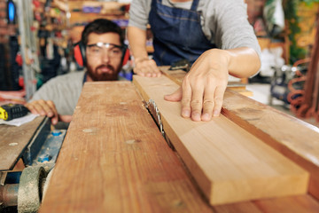 Skilled carpenters cutting wooden plank with circular saw, selective focus