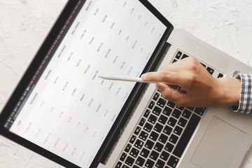 close up businessman hand with pan looking through the details of stock market on laptop