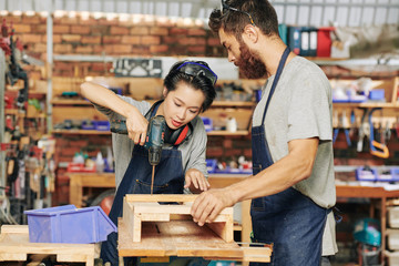 Carpenter holding wooden pieces when his coworker screwing wooden pieces together