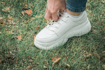 Close up legs of woman dressed in jeans and sneakers step on the grass.