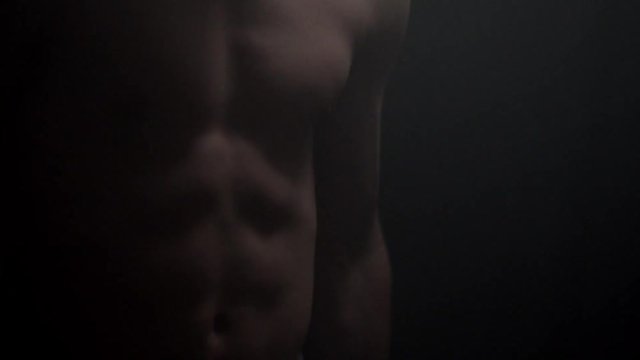 Closeup of a man abs while training and lifting weights dumbbell. Healthy lifestyle. Dark room with smoke.