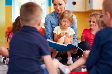 Teacher and children reading a book in the preschool
