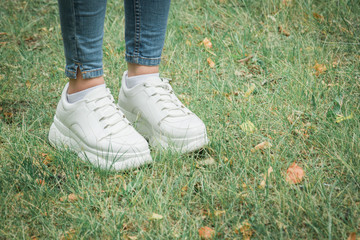 Close up female feet in sneakers on green grass in the park
