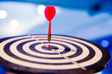 Red dart arrow hitting in the target center of dartboard on bullseye for Business focus concept.