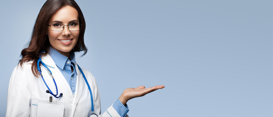 Female doctor showing something or blank copy space for slogan or sign text, isolated against grey background
