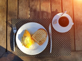 Breakfast outdoors. An omelet and toast on a white plate, a cup of coffee, salt and pepper are on the table. Cutlery lie nearby