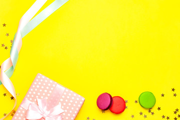 Gift or present box, beautiful festive ribbon, cake macaron or macaroon, confetti on yellow background top view. Flat lay composition for celebration, birthday, Valentine's Day, March 8, mother day