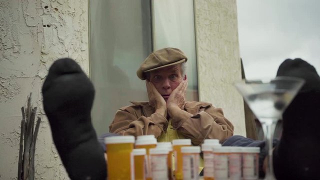 Baby Boomer Old Man With Feet On Table, Pill Bottles In-between And Glass Of Martini, Holding Face With Both Hands In Exasperation