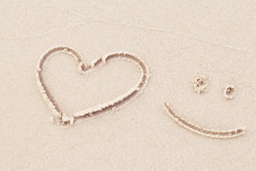 Top view of drawing heart and smile on white sand beach in background.