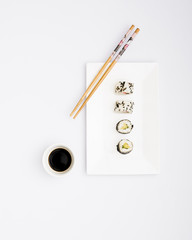 Ready to eat sushi rolls on white plate with chopsticks and soy sauce isolated over white background