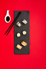 Tasty hot sushi rolls served with soya sauce on slate stone and chopsticks over red background