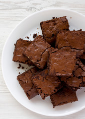 Homemade chocolate brownies on a white plate on a white wooden surface, top view. Flat lay,...
