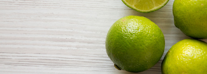 Green citrus limes on a white wooden surface, top view. From above, overhead, flat lay. Copy space.