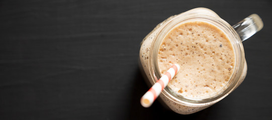 Banana, kiwi, apple smoothie in a glass jar mug over black background, top view. Flat lay, from above, overhead. Copy space.
