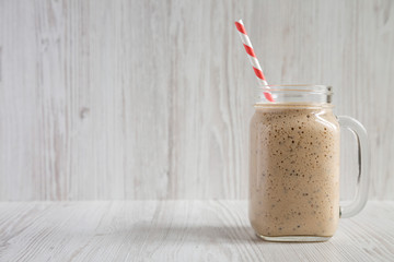 Homemade banana, kiwi, apple smoothie in a glass jar over white wooden surface, side view. Space for text.