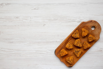 Fried camembert on a rustic wooden board on a white wooden surface, top view. Flat lay, overhead, from above. Copy space.