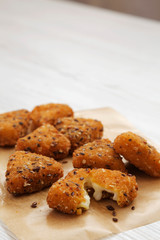 Fried camembert on a baking sheet on a white wooden surface, side view. Copy space.
