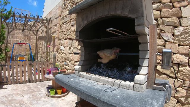 Rotisserie Chicken rotating in a wood and charcoal fire brick bbq grilling in fast forward