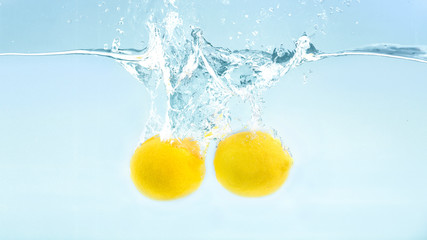 Fototapeta na wymiar Two fresh yellow lemons falling deeply into water