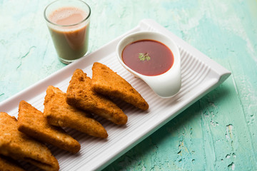 crispy Potato triangles or batata vada covered with bread crumbs and then deep fried. served with tomato ketchup. selective focus