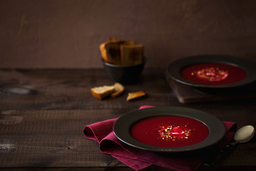 Obraz na płótnie Canvas Healthy red beet soup or smoothie decorated with chopped pistachios and sour cream in the black plate in rustic style with copy space for text. Vegetarian lunch or dinner. Horizontal orientation