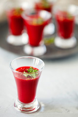 Vegetarian soup or smoothies of red beets in shot glass and decorated with chopped parsley and garlic served at a banquet or party. Close-up, vertical orientation