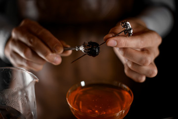 Professional bartender putting berry on the skewer with tweezers