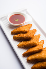 crispy Potato triangles or batata vada covered with bread crumbs and then deep fried. served with tomato ketchup. selective focus