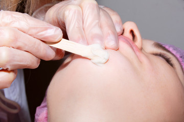 Young woman receiving facial epilation close up. Cosmetologist removes hair on face. Beauty salon, mustache depilation