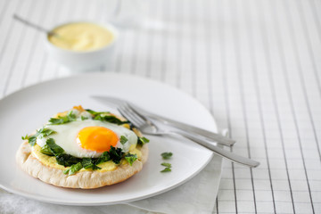 Healthy homemade breakfast or brunch (quick meal)-spiced fried eggs with Indian spices and sauteed spinach used to top toasted pitas spread with turmeric yogurt on white plate with copy space.