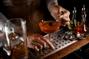 Male bartender putting berry on the skewer on the cocktail glass