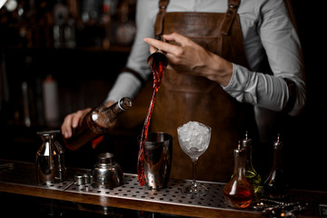 Bartender pouring a red alcoholic drink from the steel jigger to the cocktail shaker