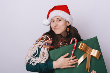 Portrait of  happy young woman wearing sant hat,  holding a big gift box, over isolated background