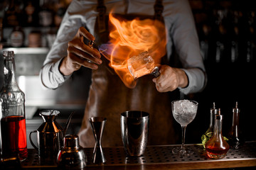 Bartender putting a fire on the big ice cube on tweezers above the steel shaker
