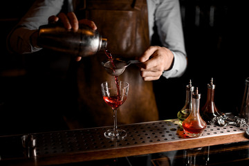 Bartender pouring a red alcoholic drink from the steel shaker through the sieve