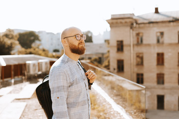 Photo of someone bearded guy,  standing on a terrace, wearing glasses, looking away and thinking