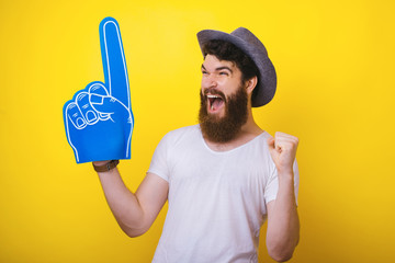 Photo of handsomea bearded guy in hat, with big blue fan glove, screaming and celebrating the...