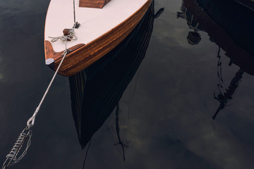 White wooden boat tie by ropes to the pier on water with reflection background